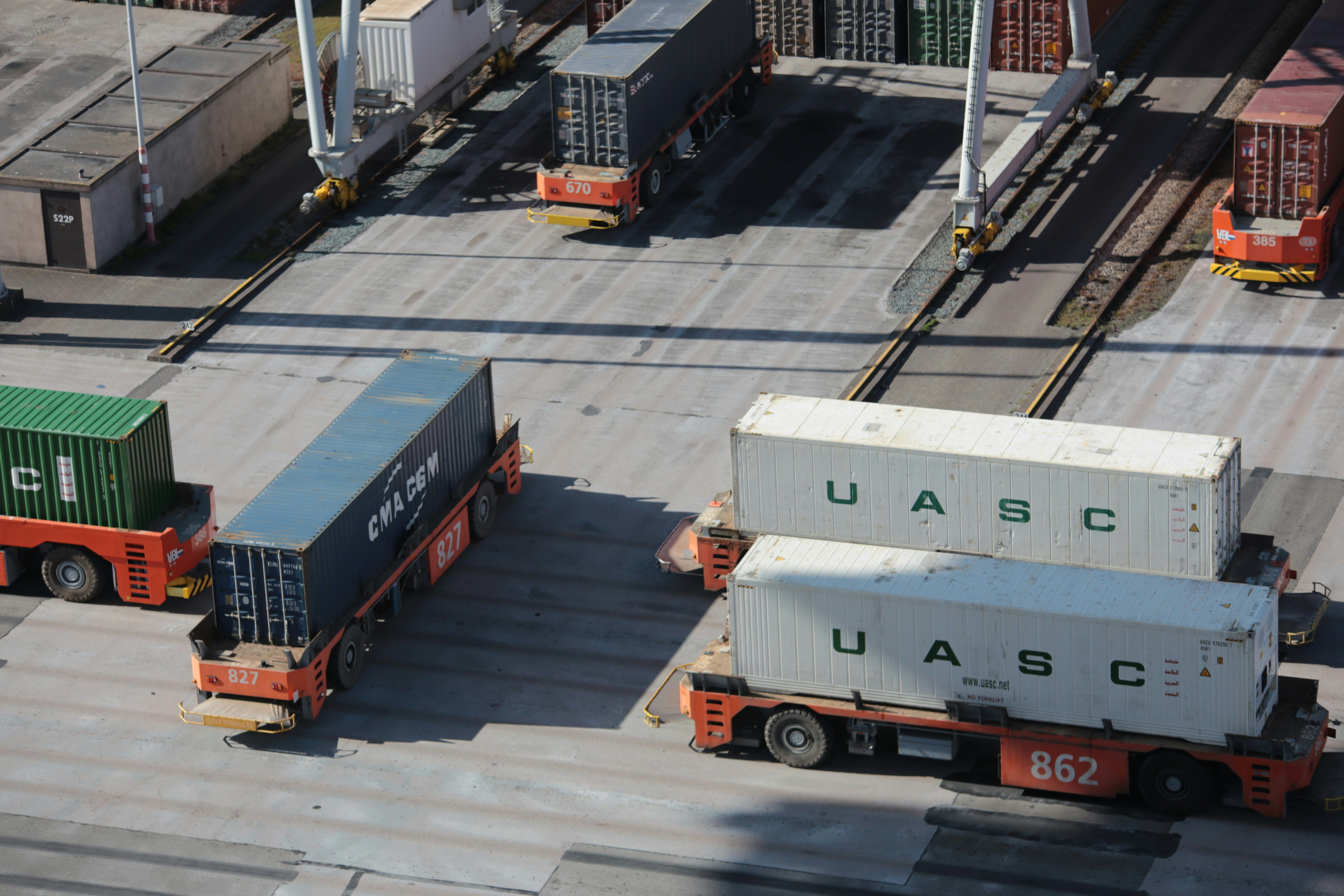 Shipping containers, including two white UASC containers, on automated transport vehicles at a port.