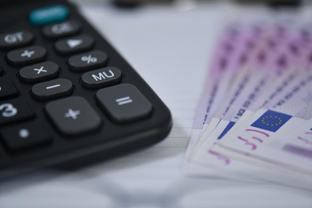 Black calculator and fanned 500 Euro banknotes on a desk.