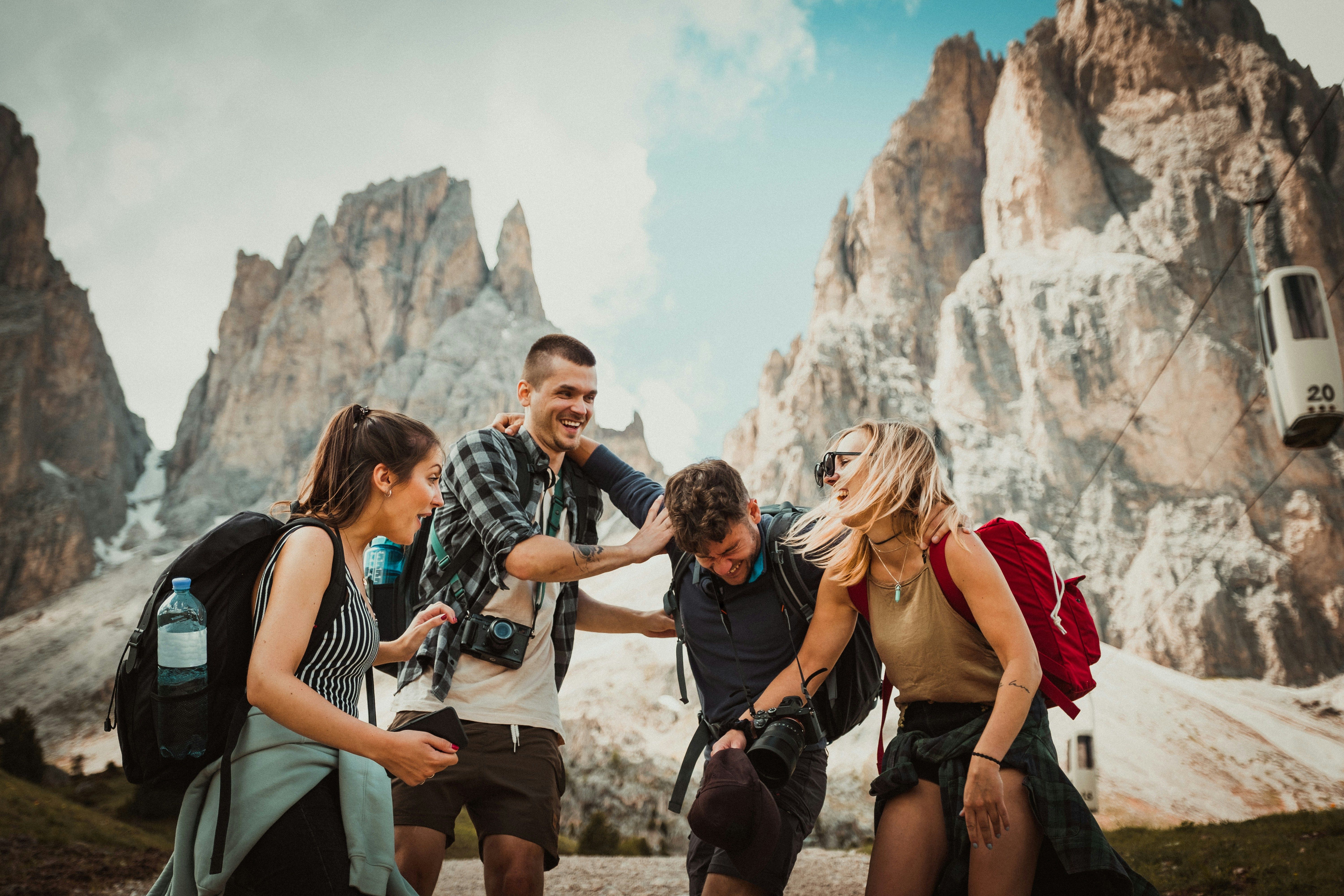 Four joyful friends laugh together in a rocky mountain landscape under a cloudy sky.