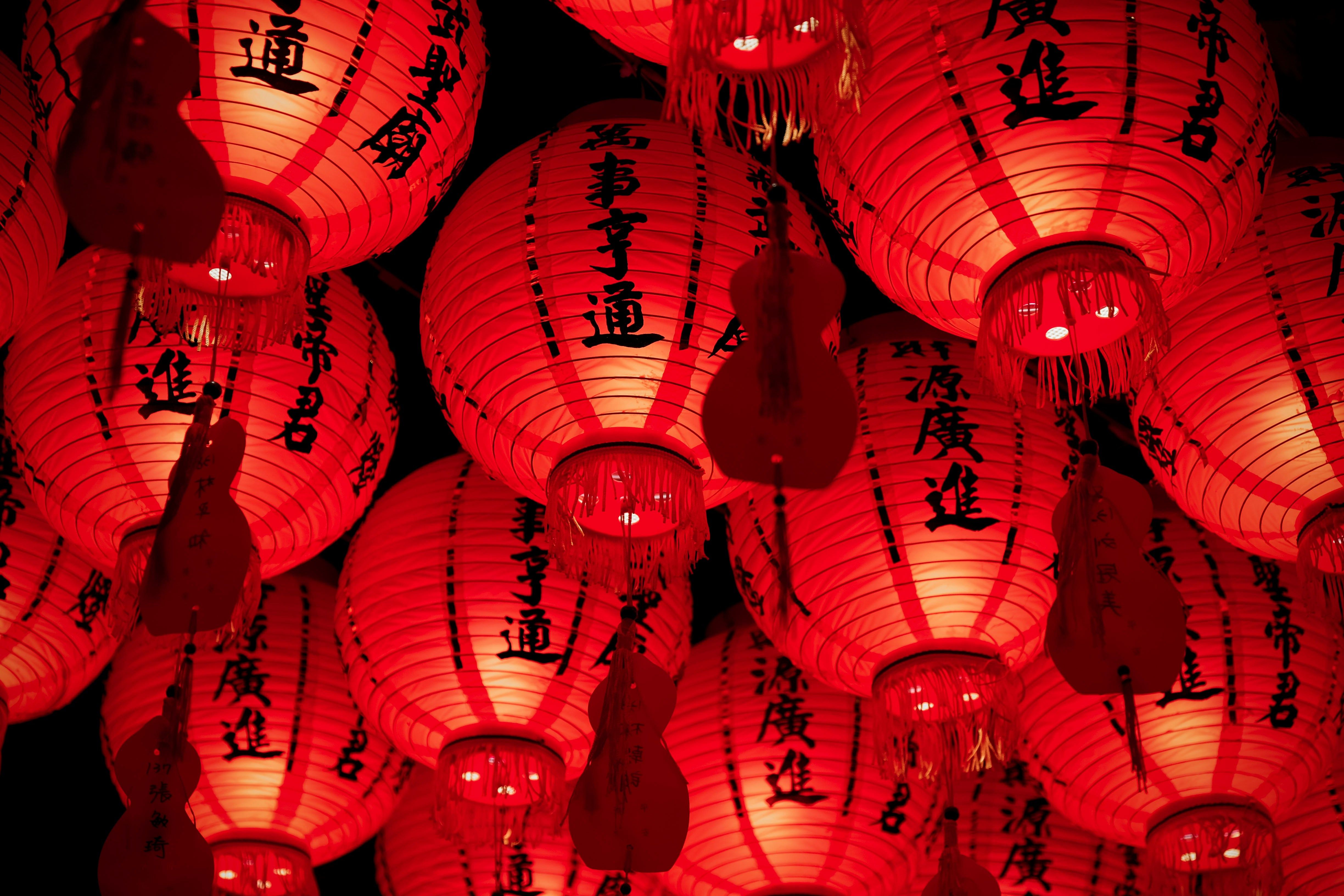 Numerous glowing red Chinese lanterns with black characters hang against a dark background.