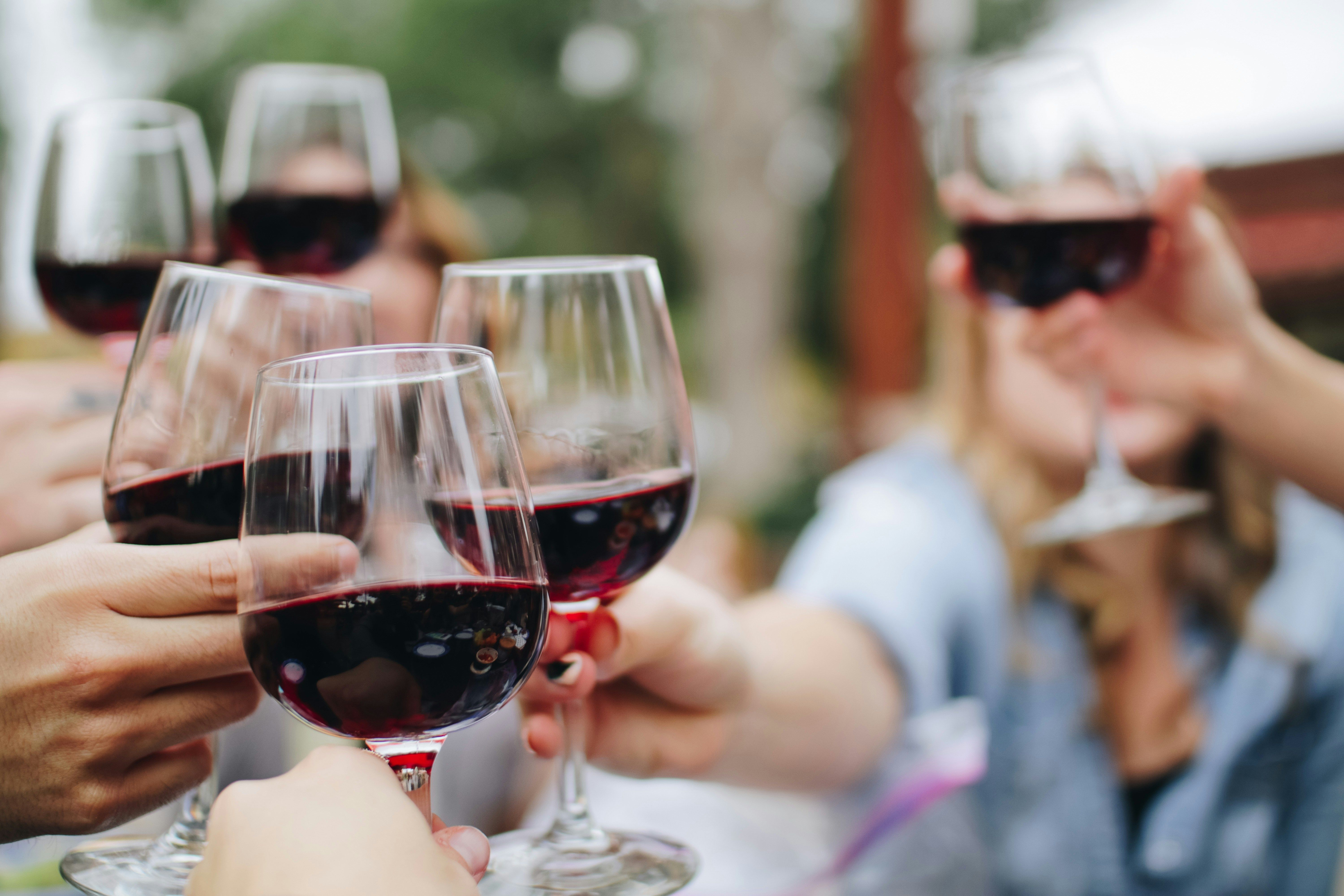 Several people clinking red wine glasses together in a toast, celebrating an event.