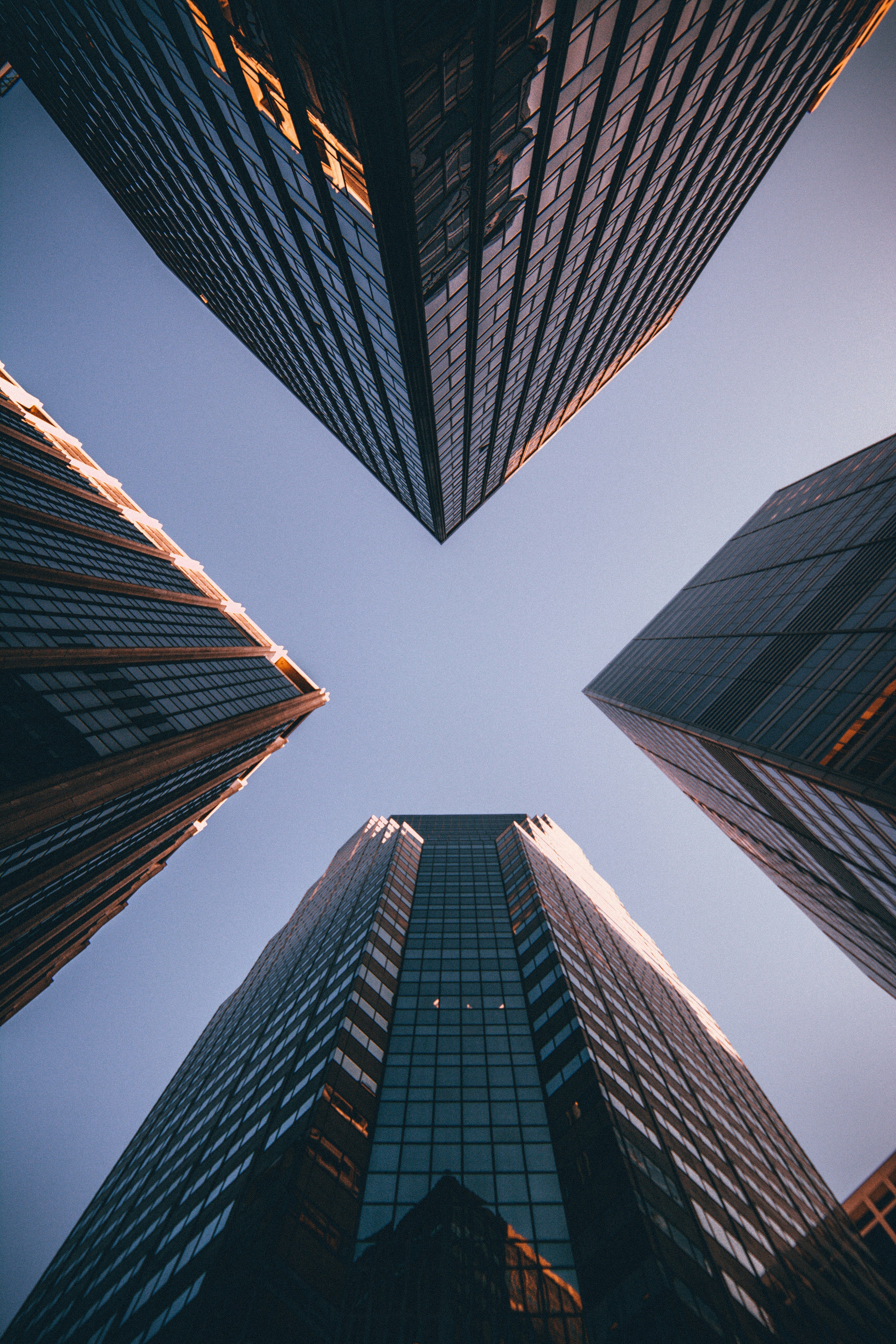 Architectural low-angle view of four modern skyscrapers converging upwards against a clear blue sky.