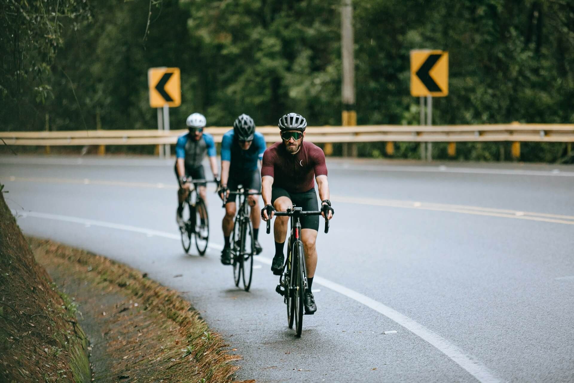 Three cyclists wearing helmets riding their bikes on a winding paved road.