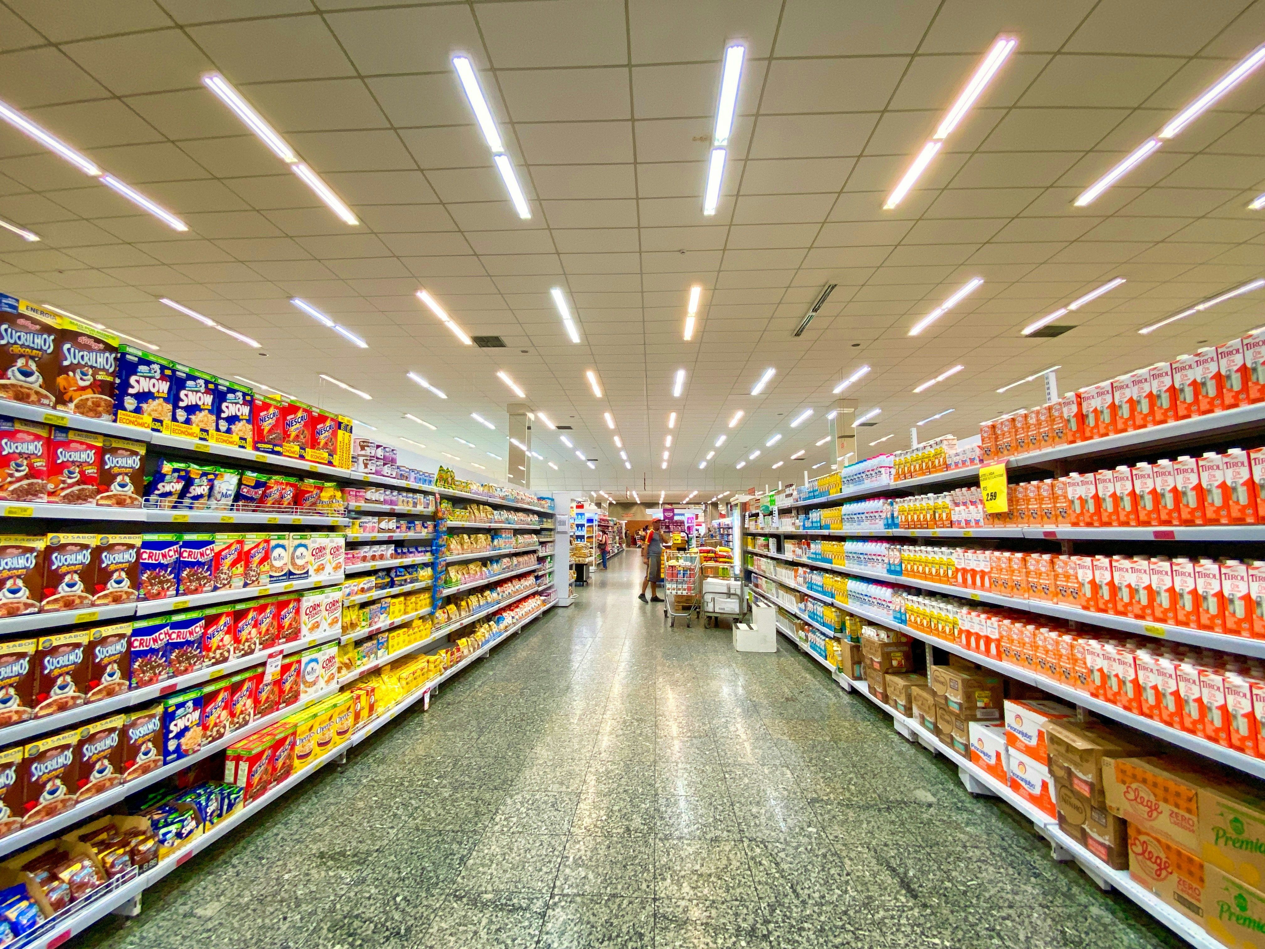 A long, brightly lit grocery store aisle with shelves full of various products.