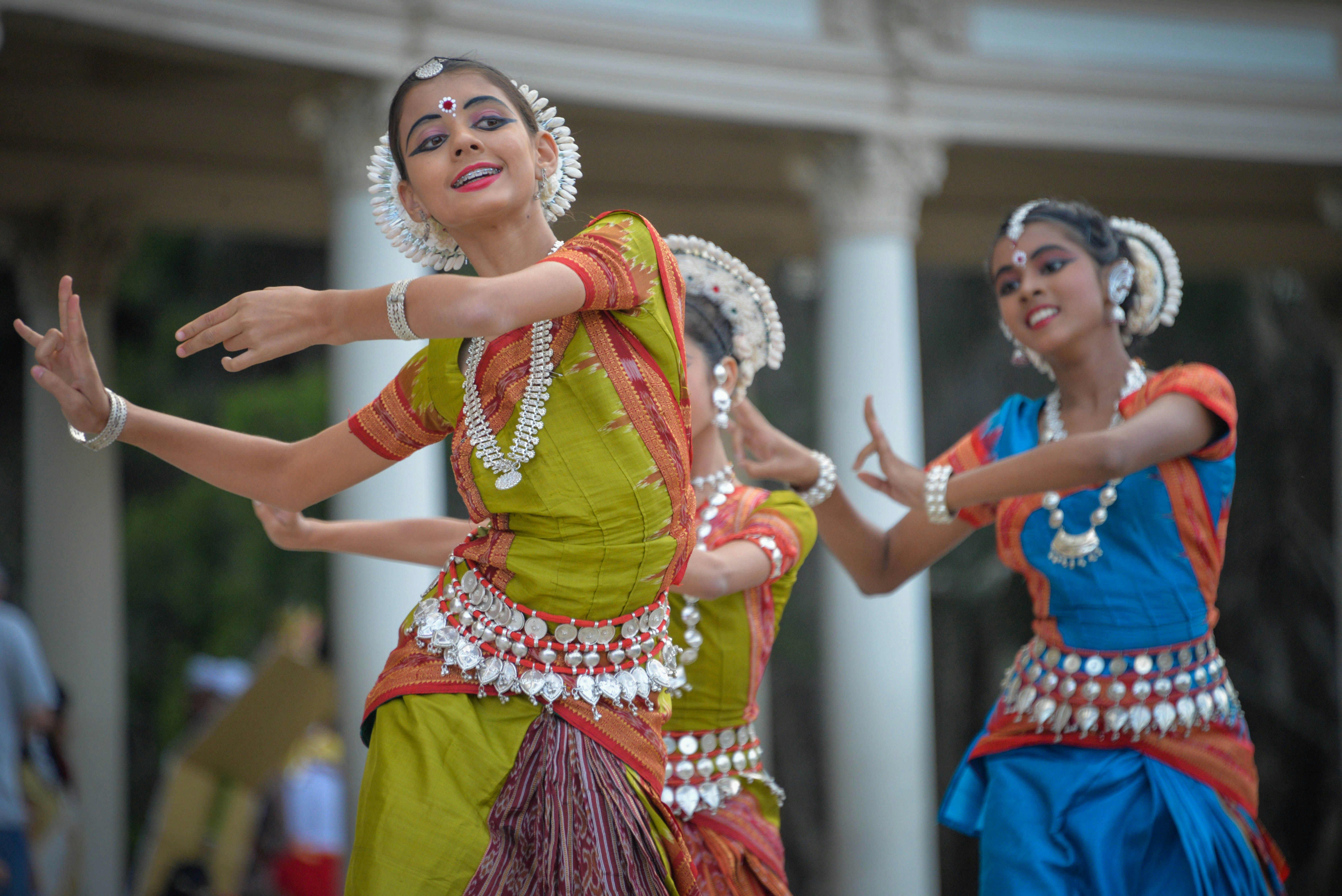Two young women in traditional Indian dance costumes perform Odissi dance outdoors.