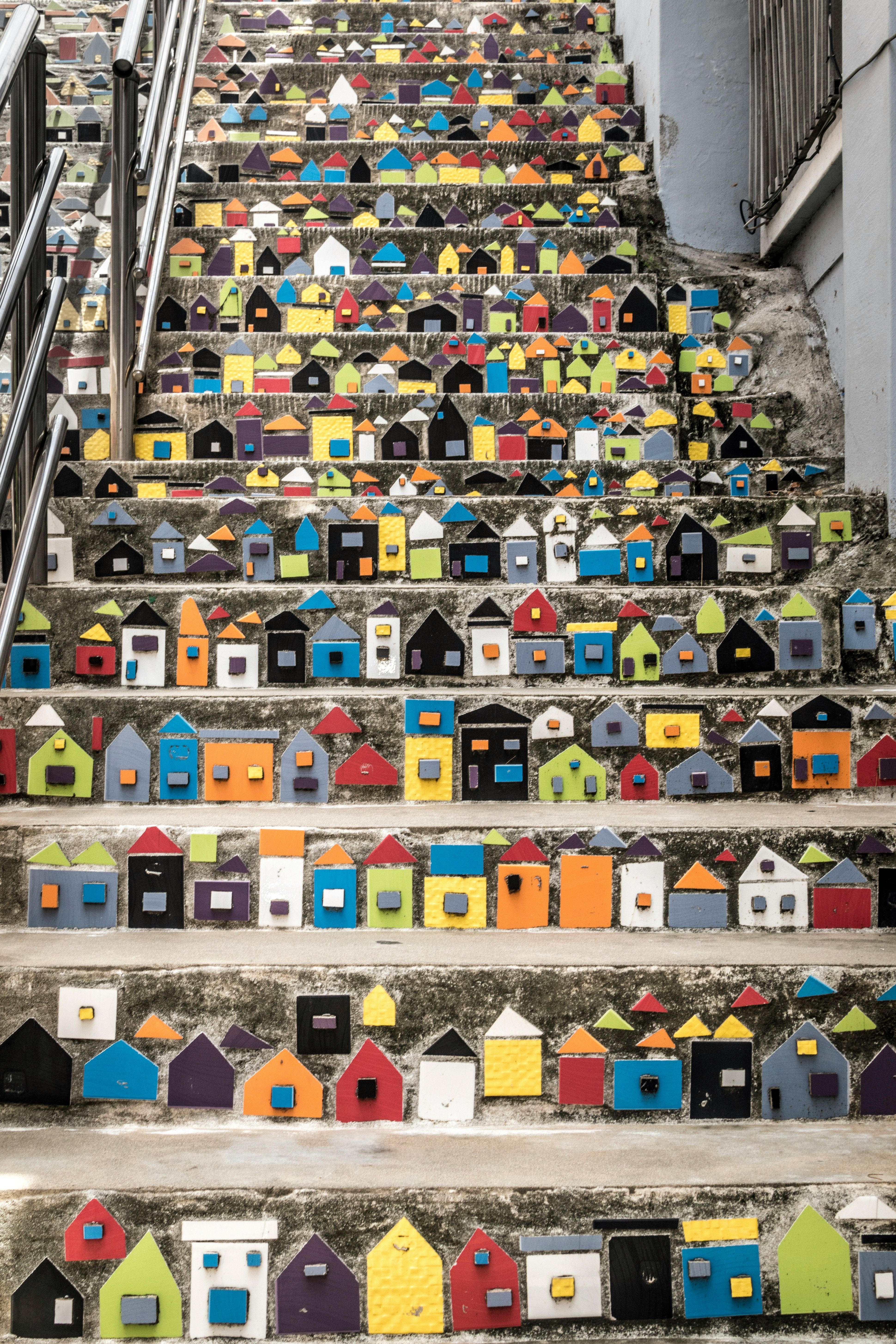 A long staircase is decorated with hundreds of colorful miniature houses, creating an art installation.